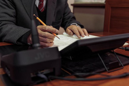 津山市議会の議場で資料に書き込みをするスーツ姿の男性議員