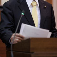 津山市議会の演壇で熱弁を振るう紺色スーツの男性議員の写真
