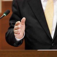 市議会で登壇する議員の身振りと市議会のマイクの写真