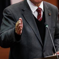 木製演壇でマイクを前に手振りで発言する議員の公式討論の風景の写真