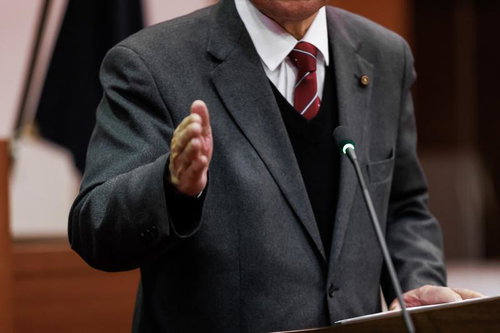 木製演壇でマイクを前に手振りで発言する議員の公式討論の風景