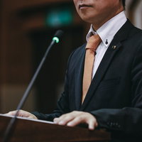 市議会の演壇でマイクの前で答弁に耳を傾ける議員の写真