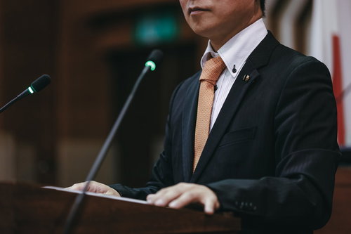 市議会の演壇でマイクの前で答弁に耳を傾ける議員