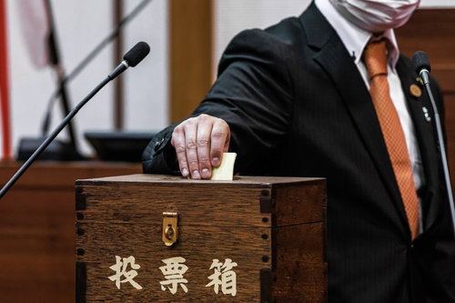 投票箱に投票用紙を投じるマスク姿の議員の