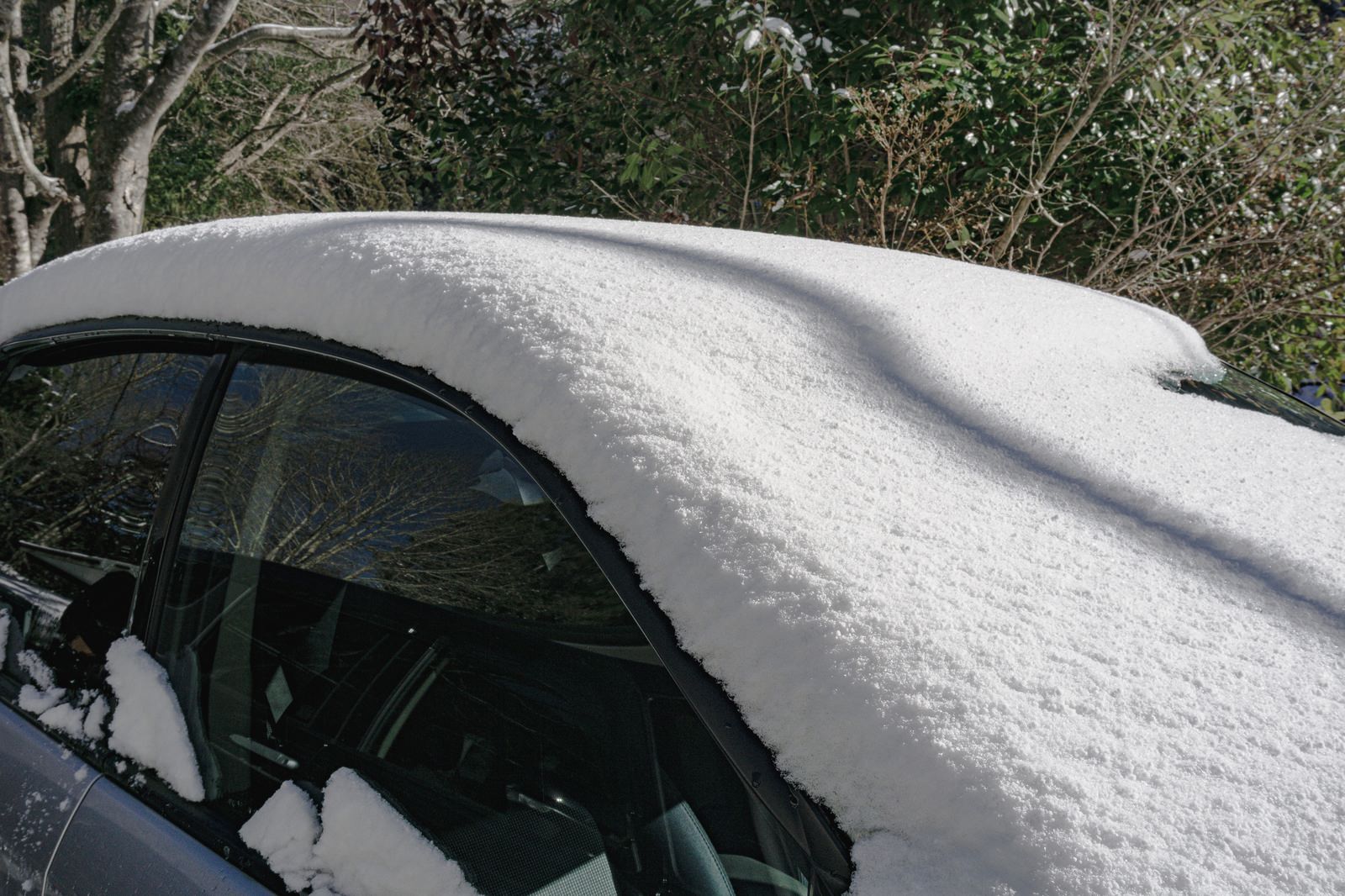 フロントガラスとサイドガラスに雪が積もった乗用車