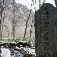 冬枯れた木々の向こうに見える戸隠山や雪の残る逆さ川を背に建つ神社御本社復興記念碑の写真
