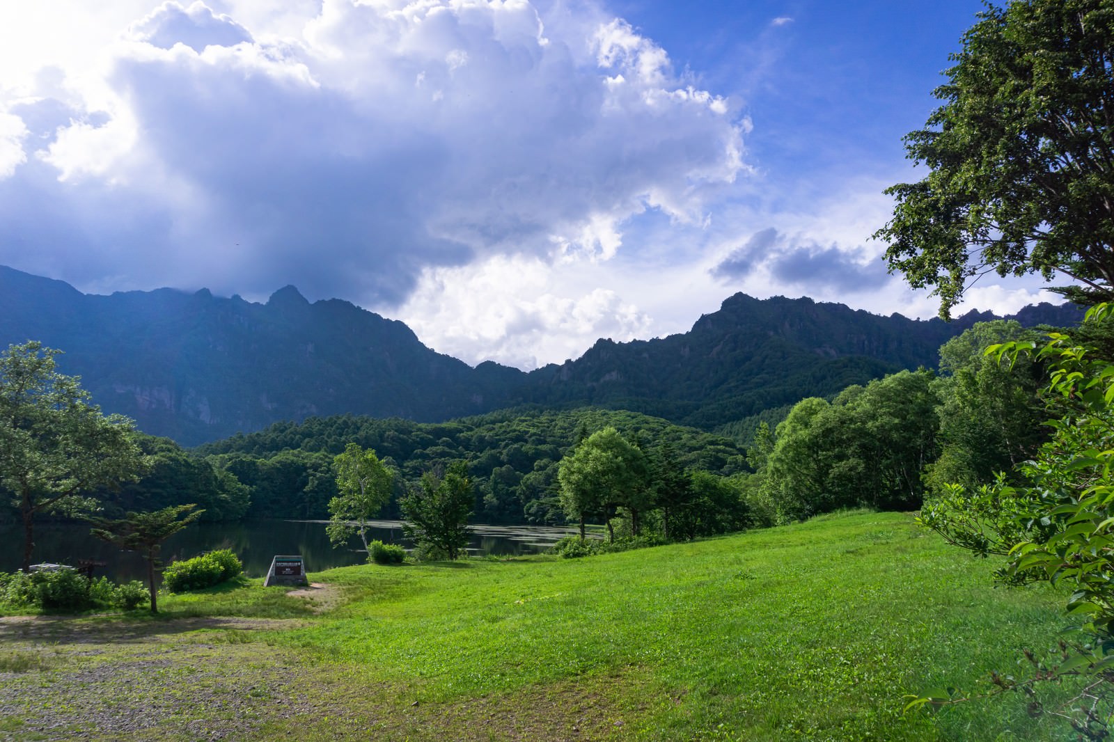 鏡池横の草地に立つ妙高戸隠連山国立公園の石碑と背景の山並み
