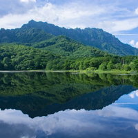 空の青さと雲の白、そして木々の緑に彩られる夏の鏡池の写真