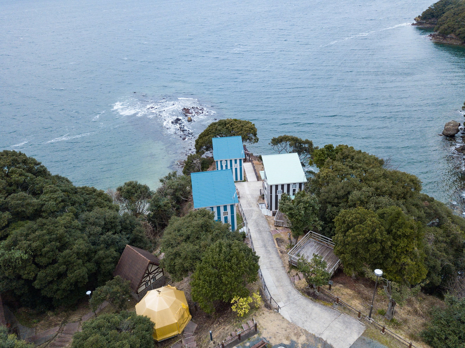 海沿いの緑地に建つ白いコテージ群を上空から撮影した崎野自然公園キャンプ場
