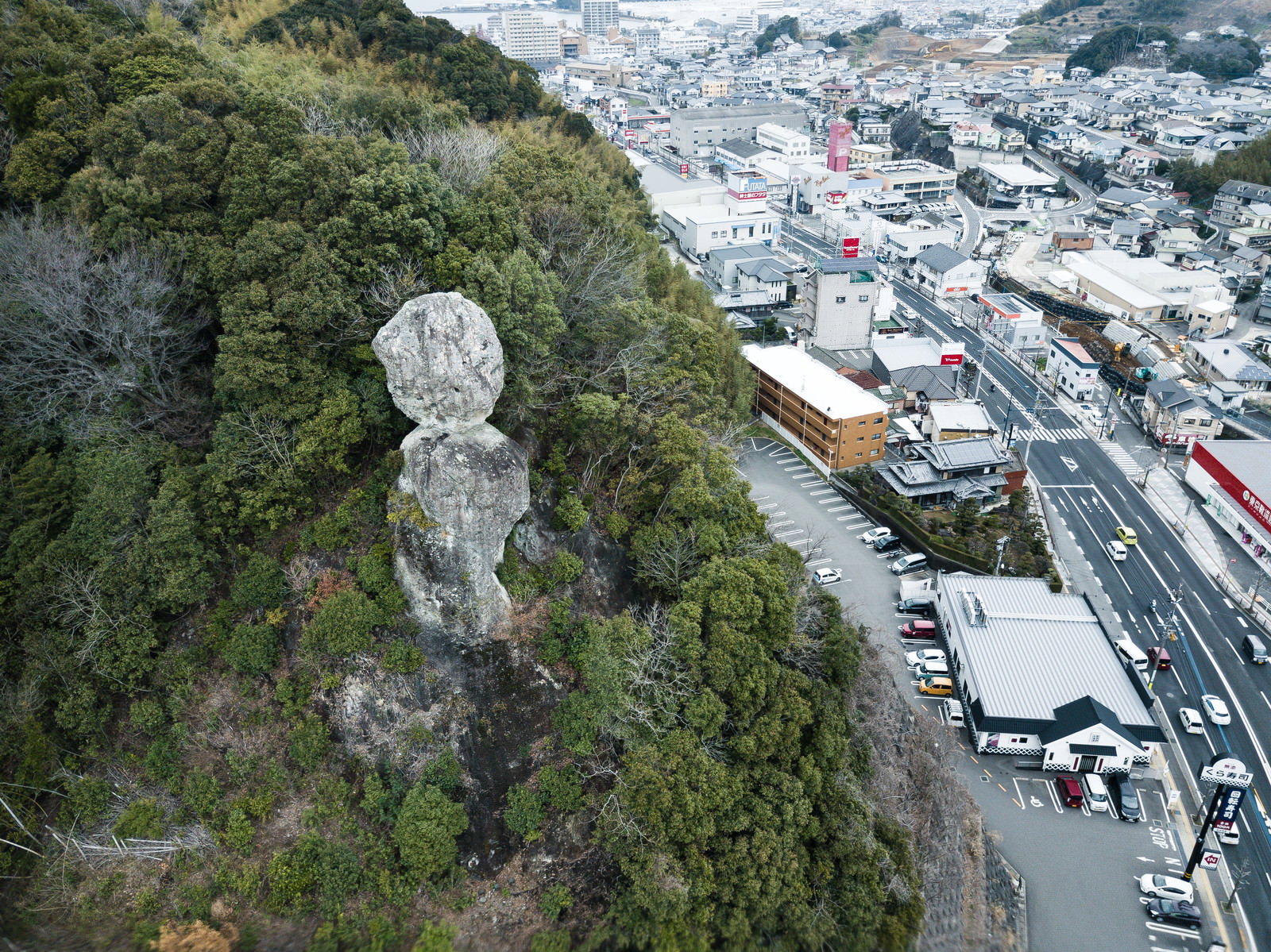 緑の山肌に不安定に佇む巨大な岩と麓に広がる住宅街の風景
