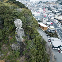 車通りが多い街中にある落ちそうな巨岩、鯖くさらかし岩の写真