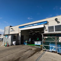 青空に映える大村湾漁業組合販売所の入り口の写真