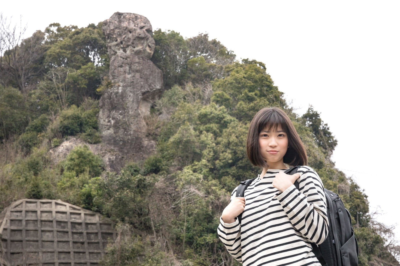 鯖くさらかし岩の前でページを探すボーダー柄の服を着た女性［モデル：塩田みう］