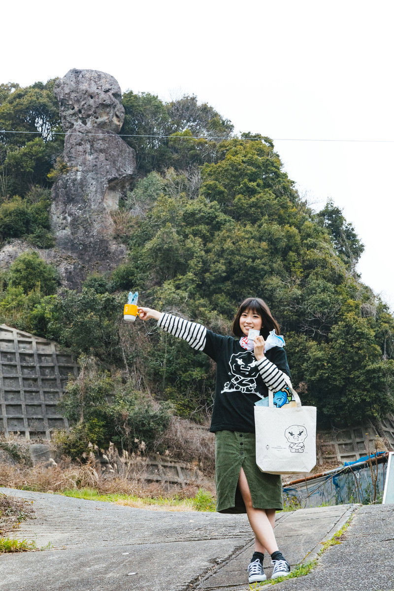 学生が岩山の前で白いグッズを掲げて手を上げ、合格を祈願している［モデル：塩田みう］
