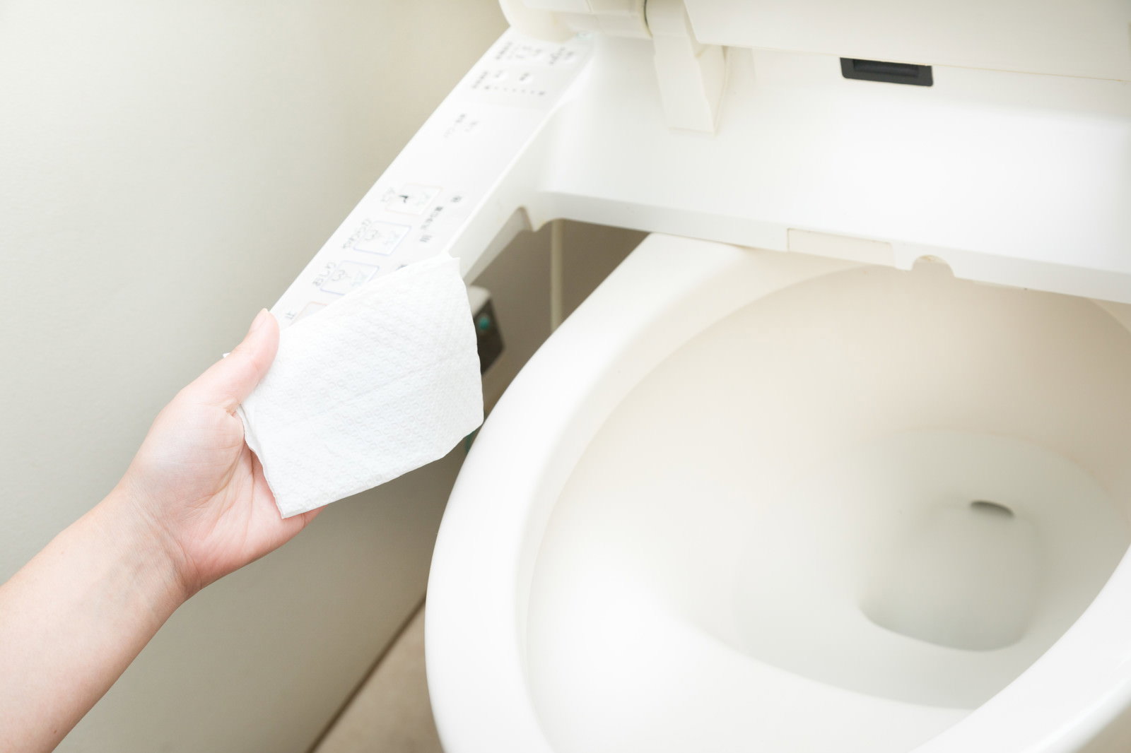 白いトイレの便座を開け、トイレットペーパーを取り出す手元