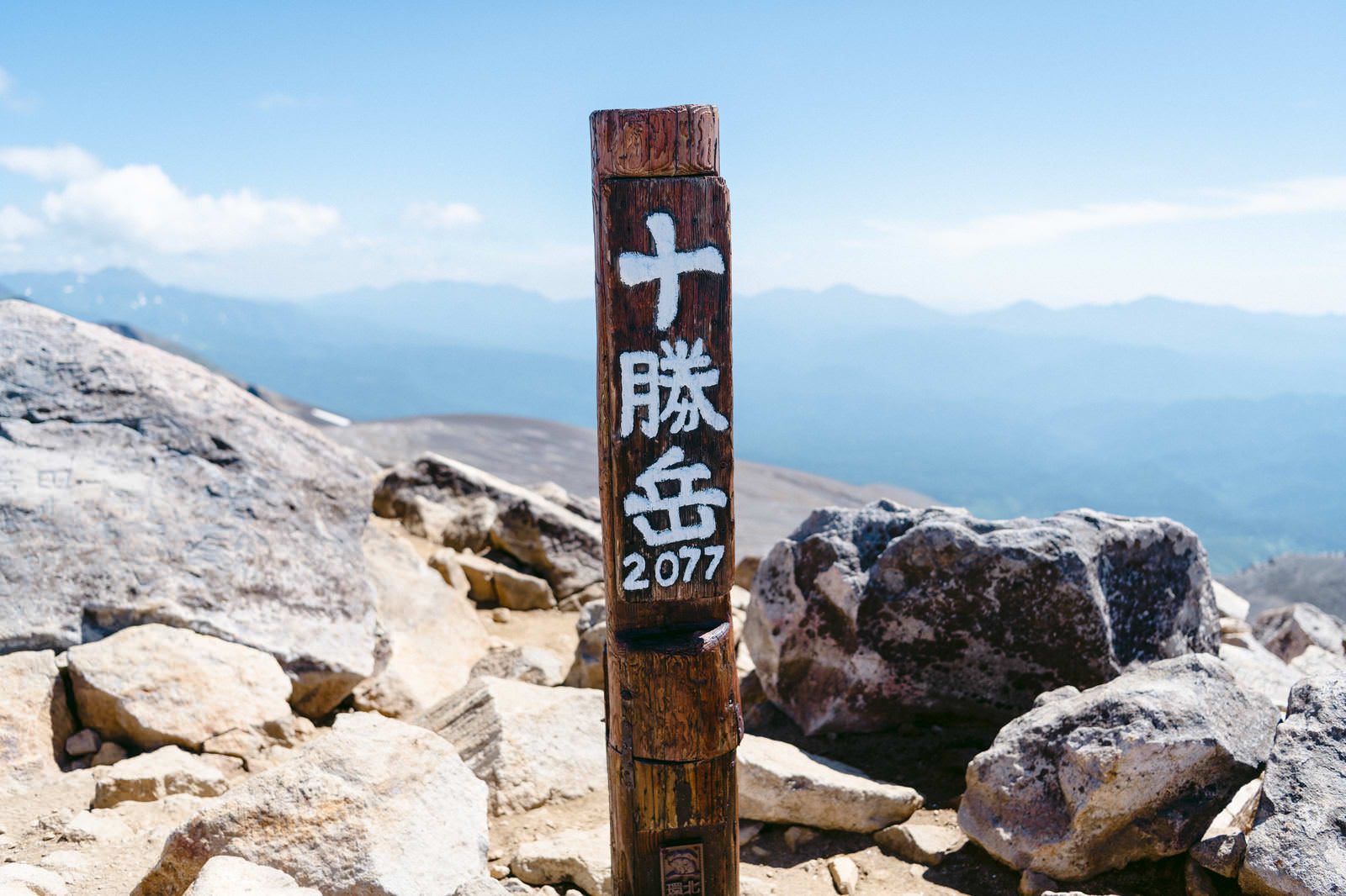 青空を背景に岩場に立つ十勝岳の木製山頂標識