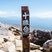 日本百名山の十勝岳山頂に立つ木製の山頂標識の写真