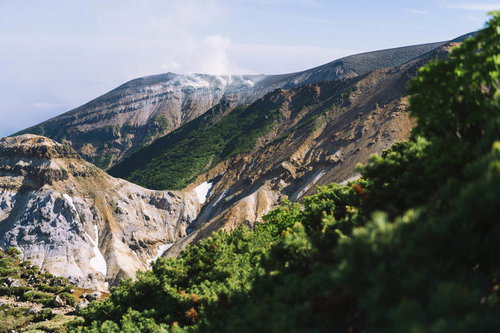 噴煙上げる十勝岳の火口と麓の緑の谷間の自然風景