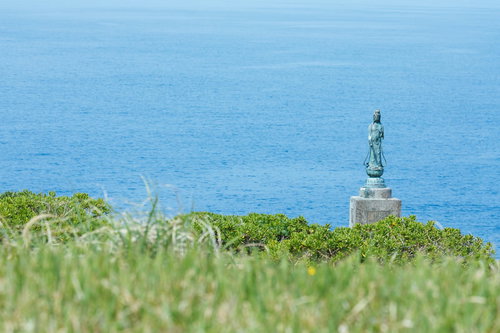 徳之島の犬の門蓋に立つ観音菩薩像と青い海の風景