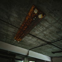 天井に設置された錆びた蛍光灯と劣化したコンクリート壁（廃墟）の写真