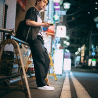 夜の野毛の繁華街でマップアプリを見て居酒屋を探す男性の写真