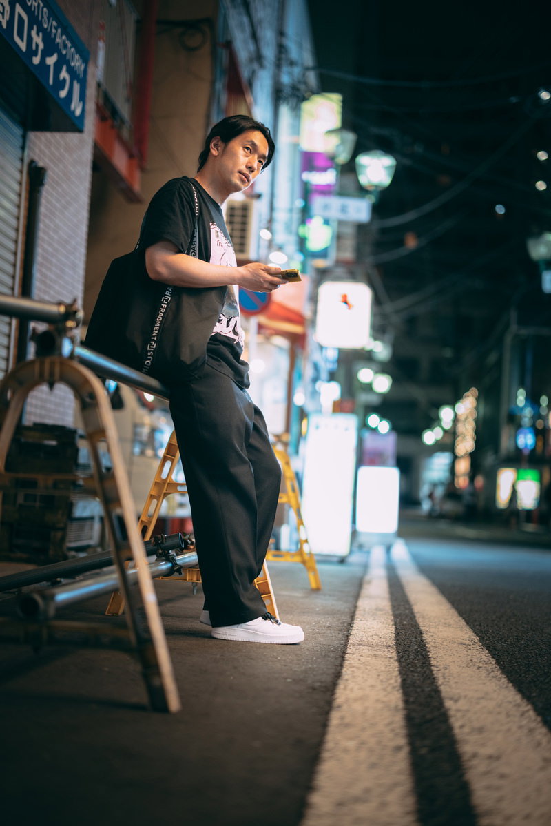 夜の繁華街でスマートフォンのマップアプリを見ながら居酒屋を探す男性［モデル：大川竜弥］