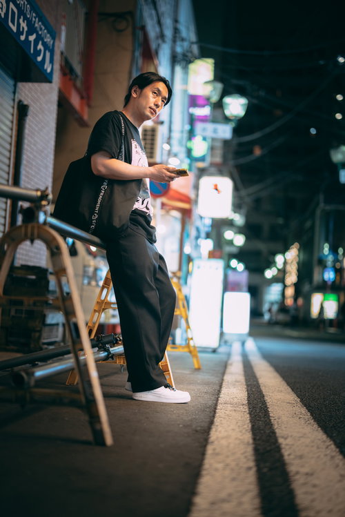 夜の野毛の繁華街でマップアプリを見て居酒屋を探す男性