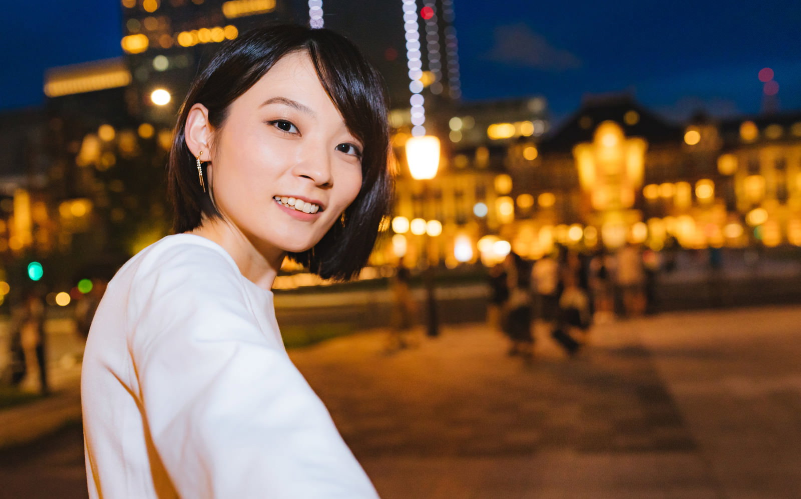 東京駅の夜景をバックに振り返る女性［モデル：たけべともこ］