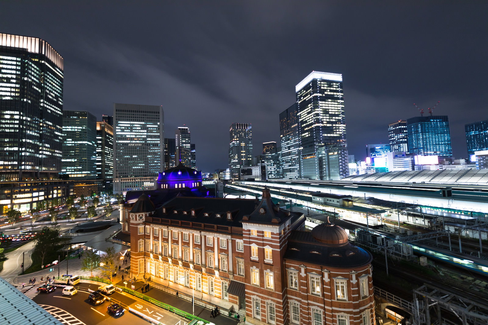 夜の東京駅丸の内駅舎と高層ビル群、手前にホームが写る夜景
