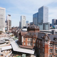 昼間の駅前で工事が続く東京駅丸の内駅舎と高層ビル群の写真