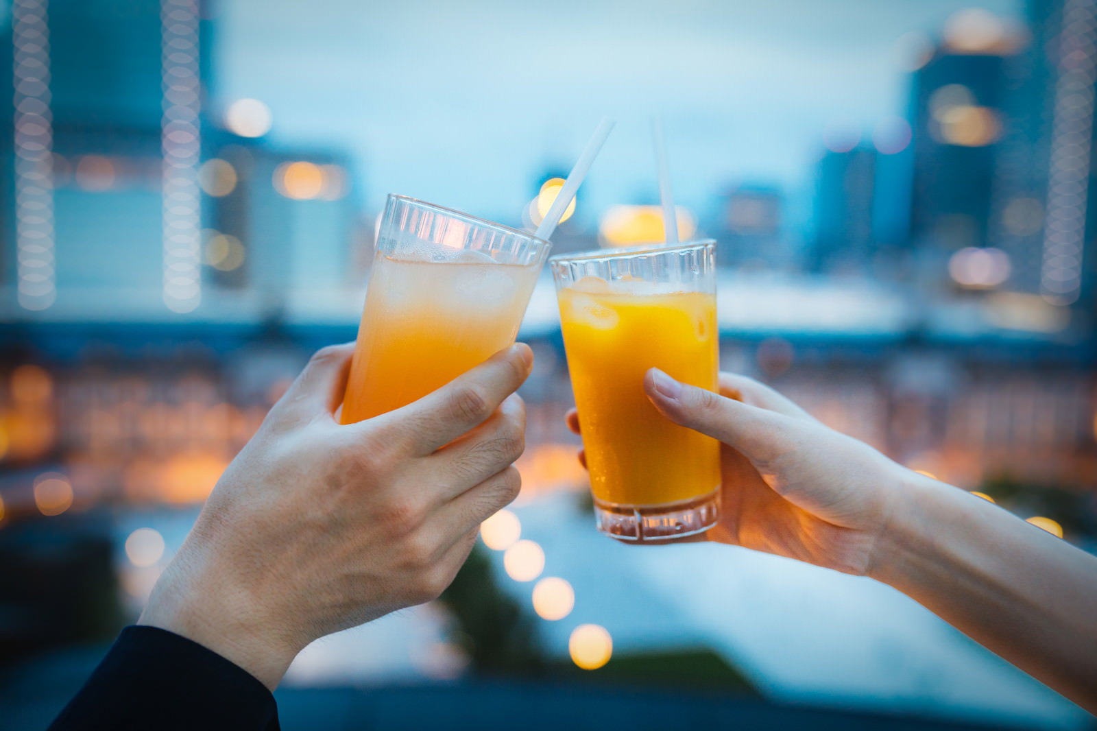 夜景をバックにオレンジ色の飲み物で乾杯するカップルの手