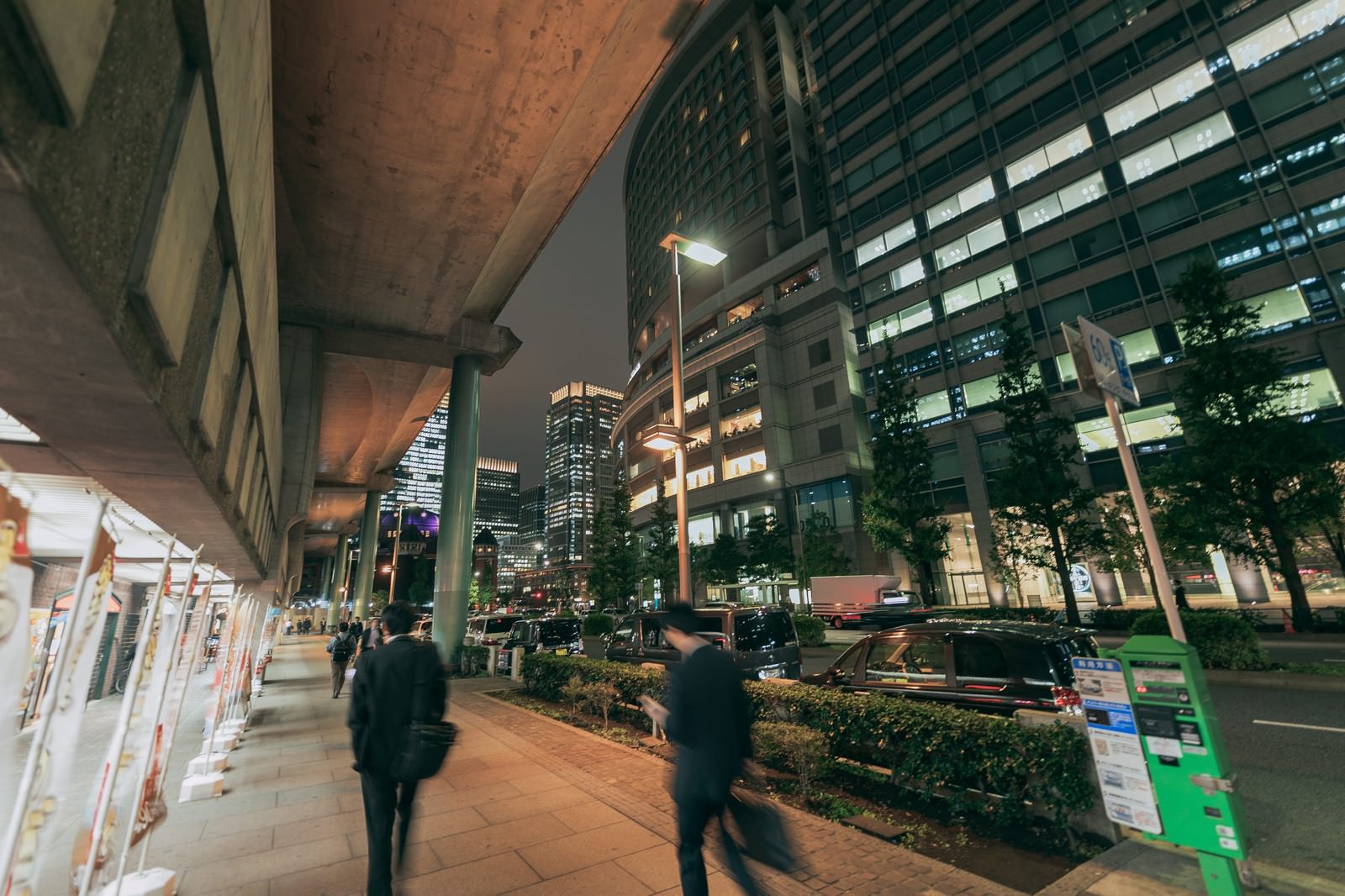 夜の丸の内で歩道を歩く会社員の後ろ姿とライトアップされたビル群