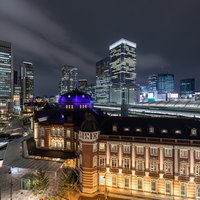 ライトアップされた東京駅の赤レンガ越しに見る丸の内ビル群の夜景の写真