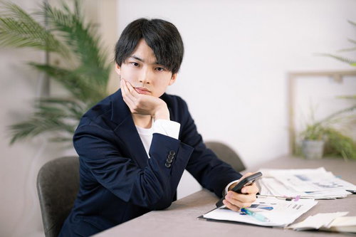 デスクでスマホを持ち考え込むビジネスパーソン