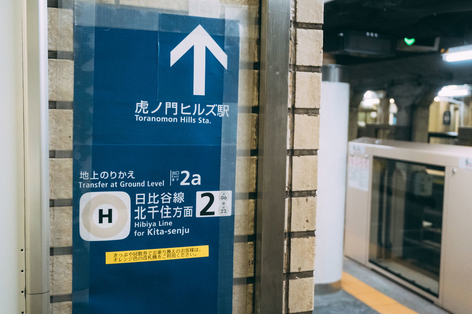 虎ノ門ヒルズ駅を示す青い矢印案内板が地下鉄ホームの柱に設置されている