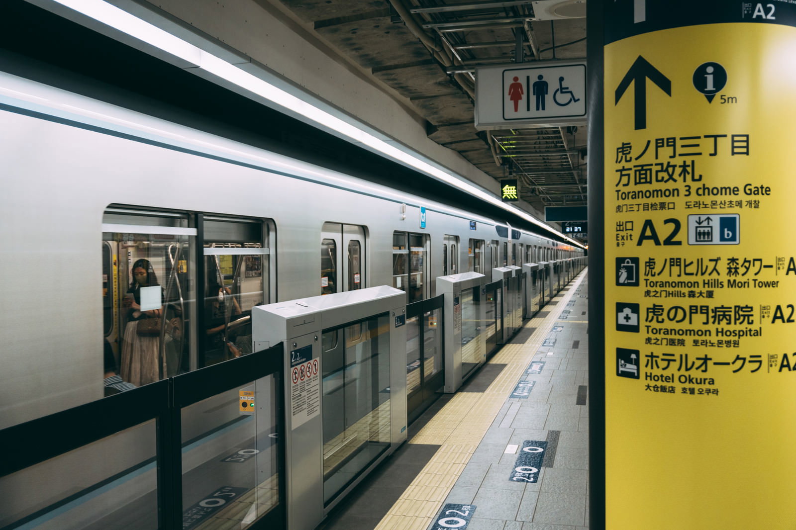 虎ノ門ヒルズ駅ホームの黄色い案内板と停車中の地下鉄車両