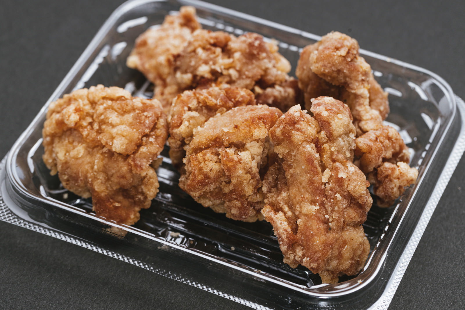 透明なプラスチック容器に入った黄金色の鶏の唐揚げ