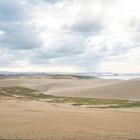 厚い雲から差す光が照らす鳥取砂丘の風景と海の写真