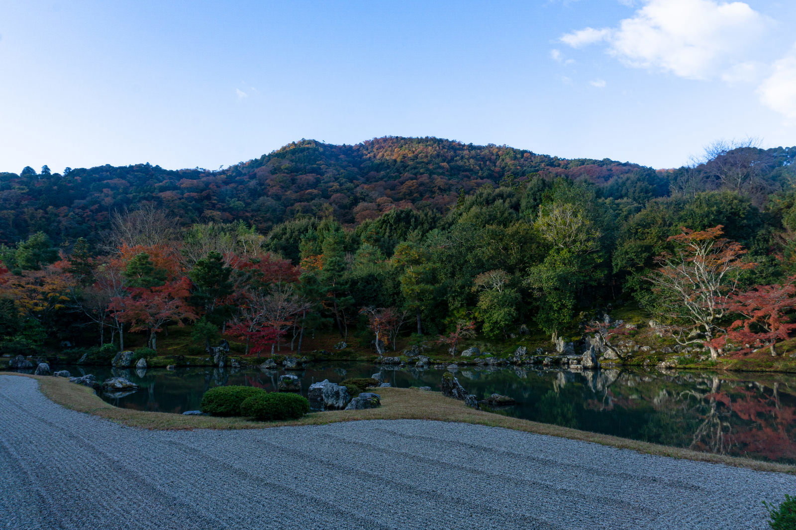 天龍寺曹源池庭園の白砂と滝石組、背景に秋の紅葉が見える日本庭園