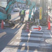ショベルカーが停車する工事中の迂回歩道と作業員による交通整理の写真