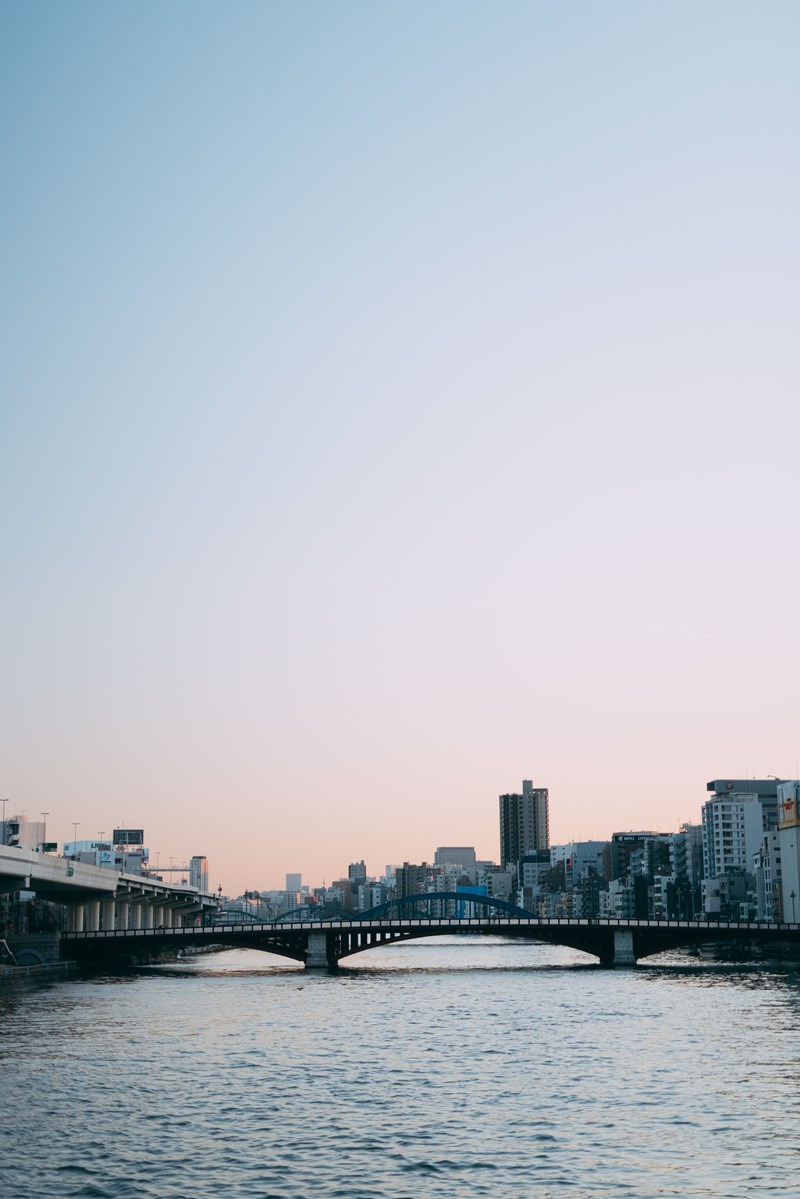 夕焼け空の下、隅田川に架かる橋と両岸の建物が水面に映る風景