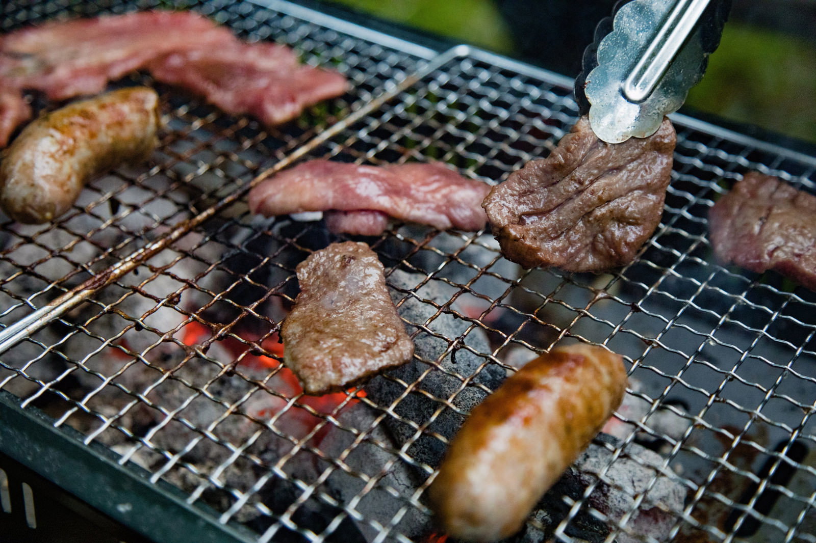 炭火の網で焼かれる肉とソーセージのバーベキュー風景