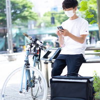 スマートフォンで配達依頼を確認する配達員の男性の写真