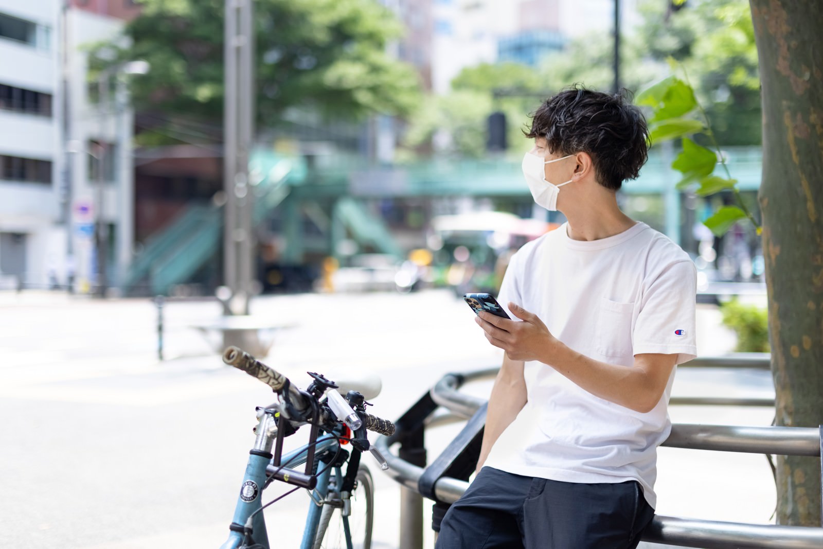 白いTシャツを着た男性が自転車の横でスマートフォンを見ている［モデル：TSURUTAMA］