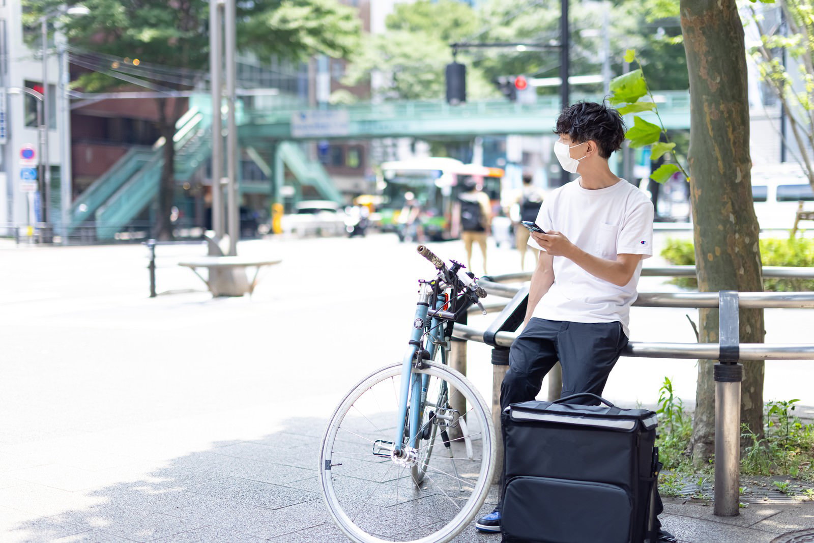 ベンチに座ってスマートフォンを操作する配達員の男性［モデル：TSURUTAMA］