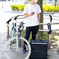 木陰で次の配達まで休憩するフードデリバリー配達員の男性の写真