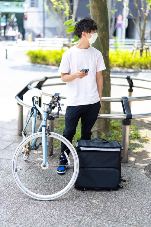 木陰で次の配達まで休憩するフードデリバリー配達員の男性