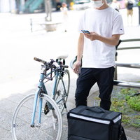 宅配用の黒いリュックを背負った配達パートナーと自転車の写真