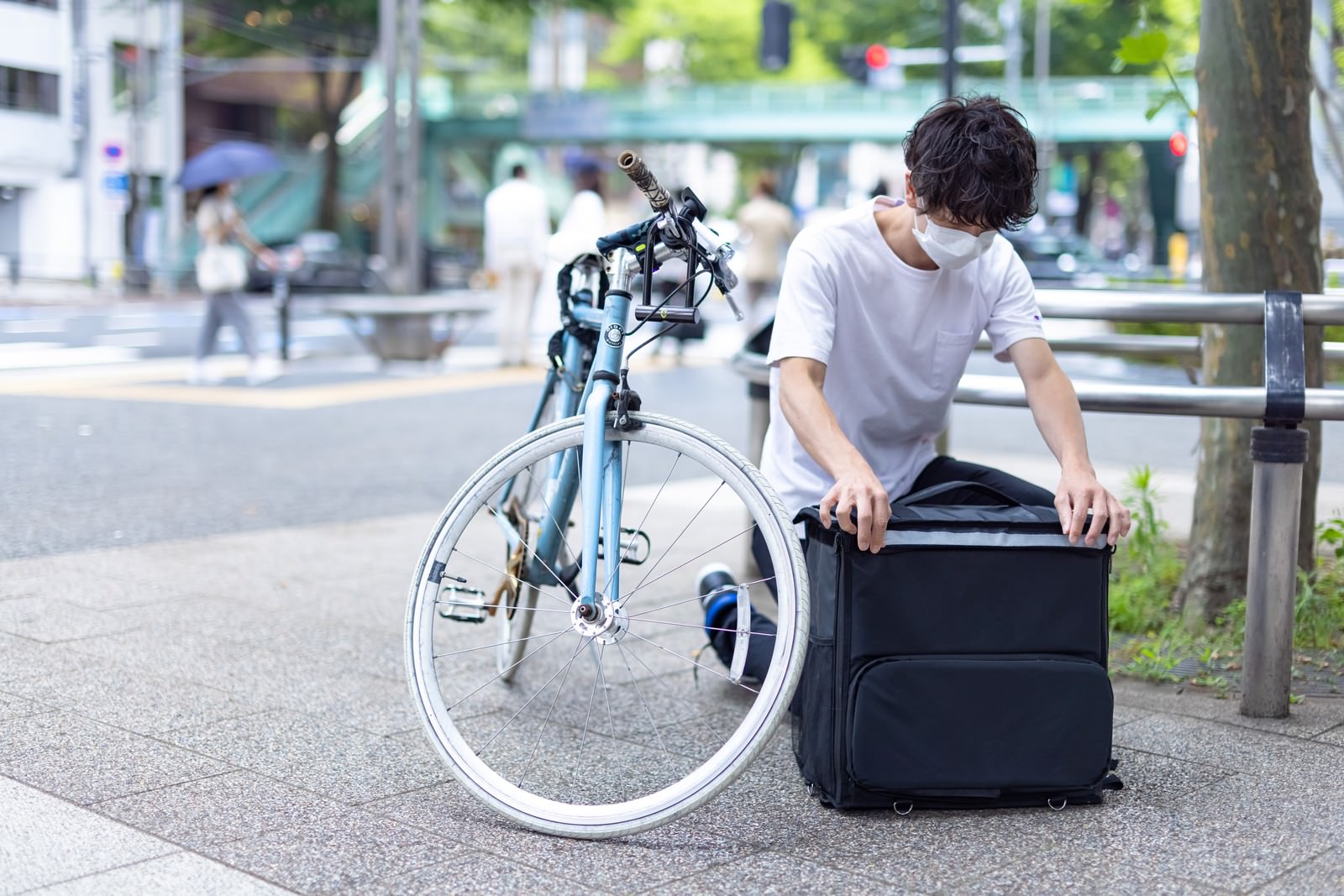 フードデリバリーの配達員が歩道でバッグを確認［モデル：TSURUTAMA］