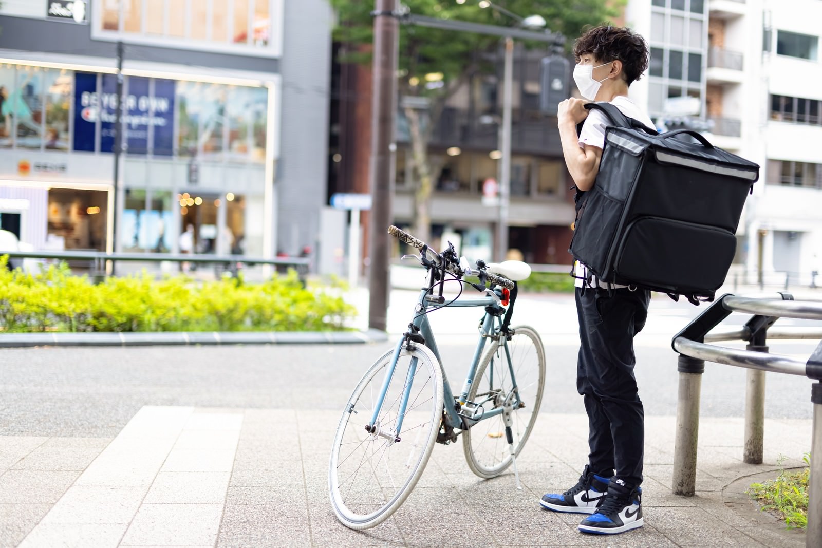 デリバリーバッグを背負い自転車のそばに立つフードデリバリー配達員の男性